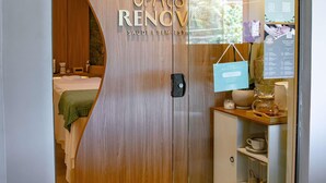 A modern hotel room with a wooden door, a bed with a green blanket, a small cabinet with toiletries, and a view of the outdoors. - Mercure Florianópolis (Florianópolis)