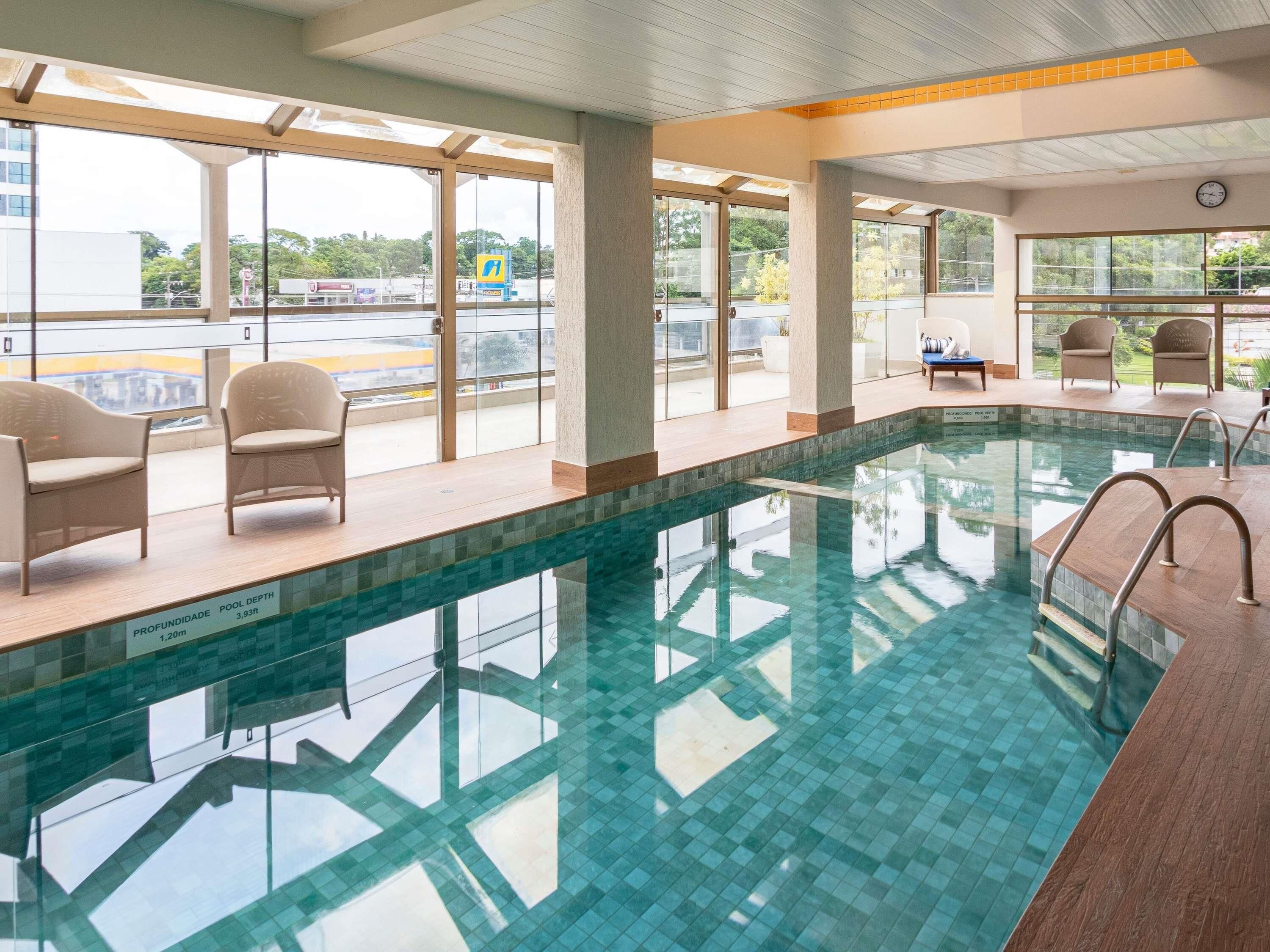 A swimming pool with clear water, surrounded by lounge chairs and a view of the outside.