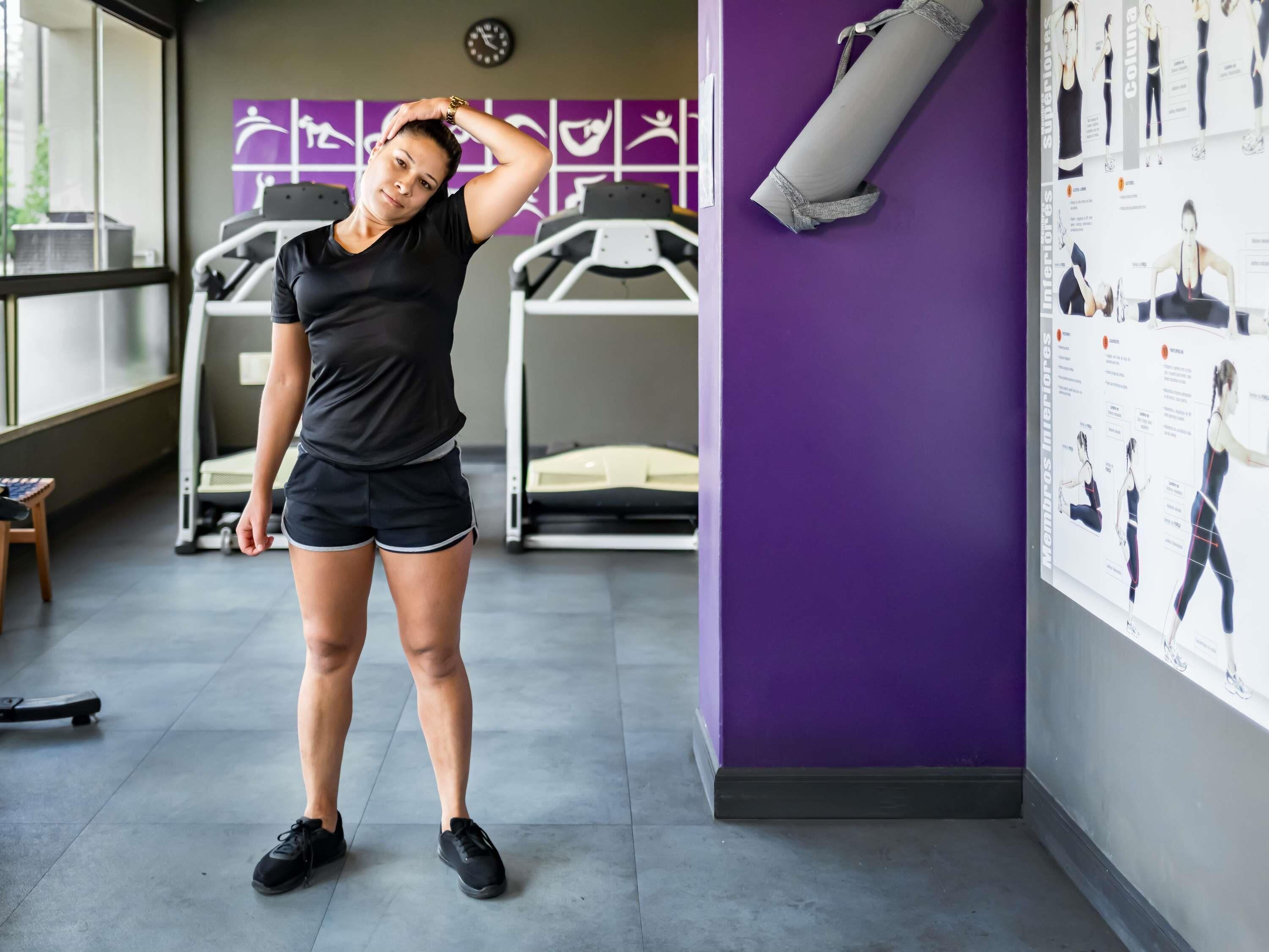 Una persona en un gimnasio con equipo de ejercicio, una pared morada con carteles y una ventana.