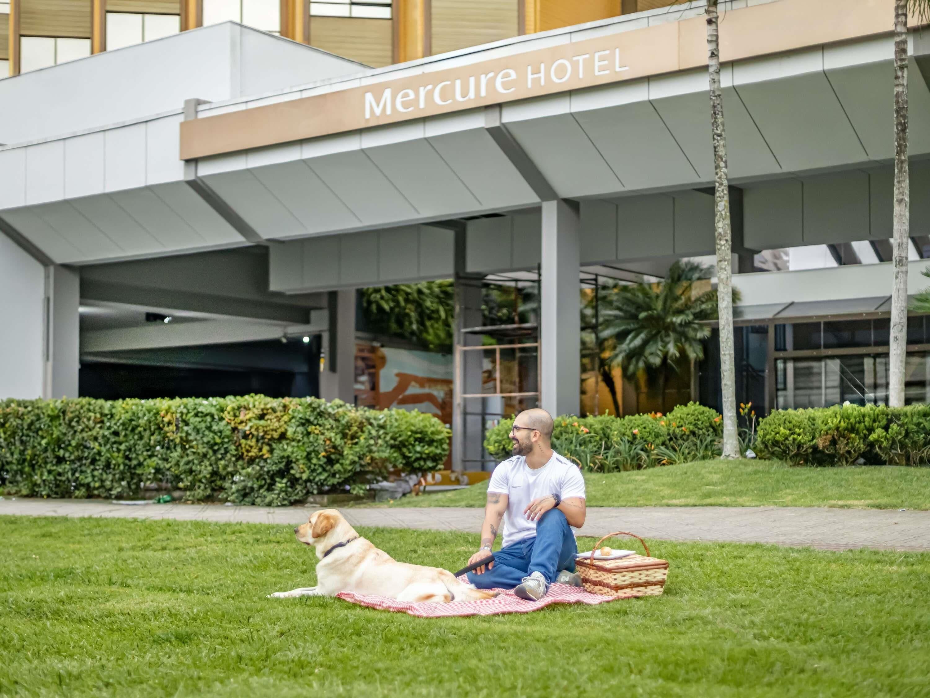 Un uomo seduto su una coperta con un cane davanti all'hotel Mercure Hotel.
