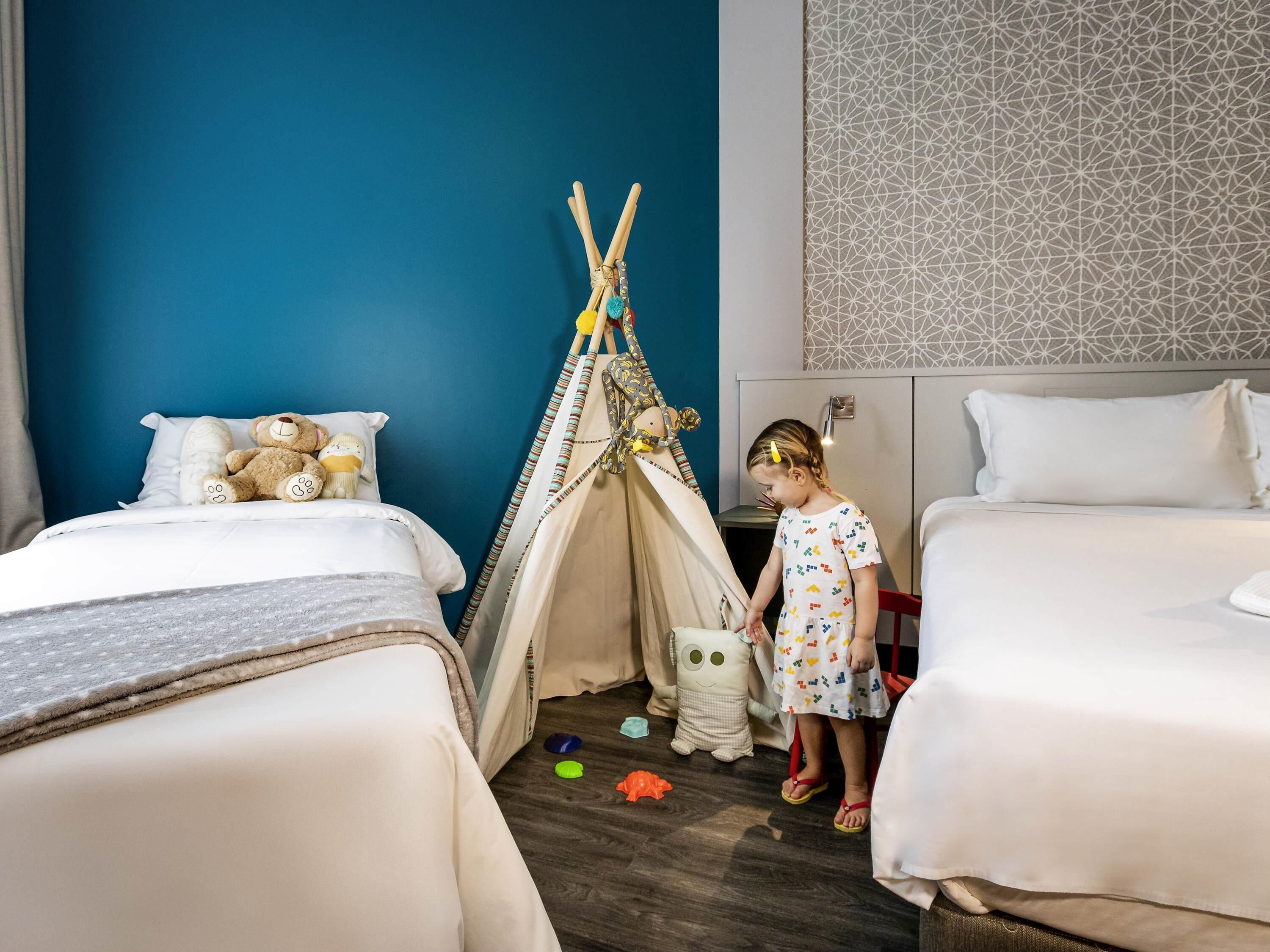Habitación infantil con dos camas, una tienda tipi y un muro con diseño geométrico.