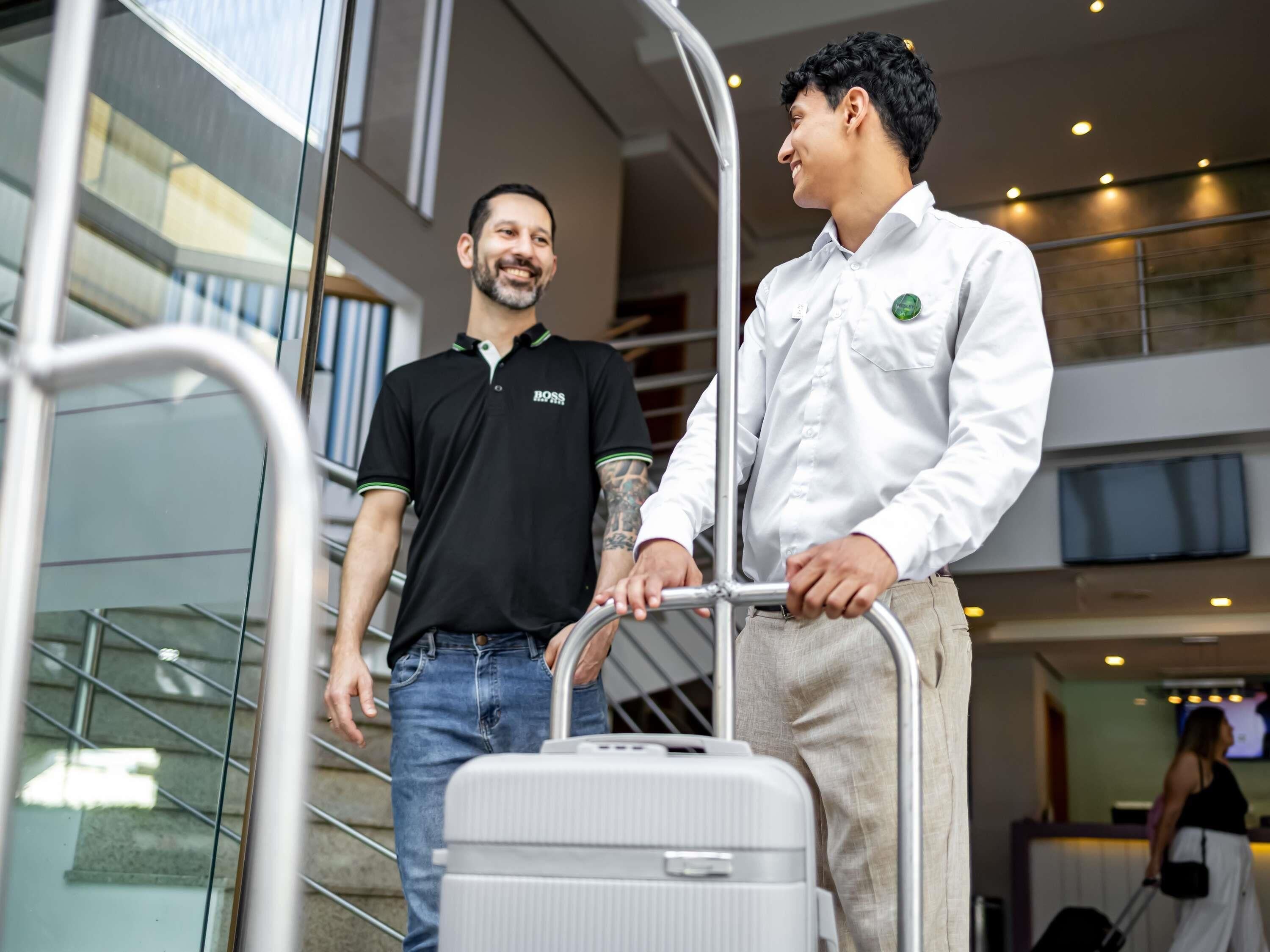 Two individuals at an airport, one pushing a luggage cart.