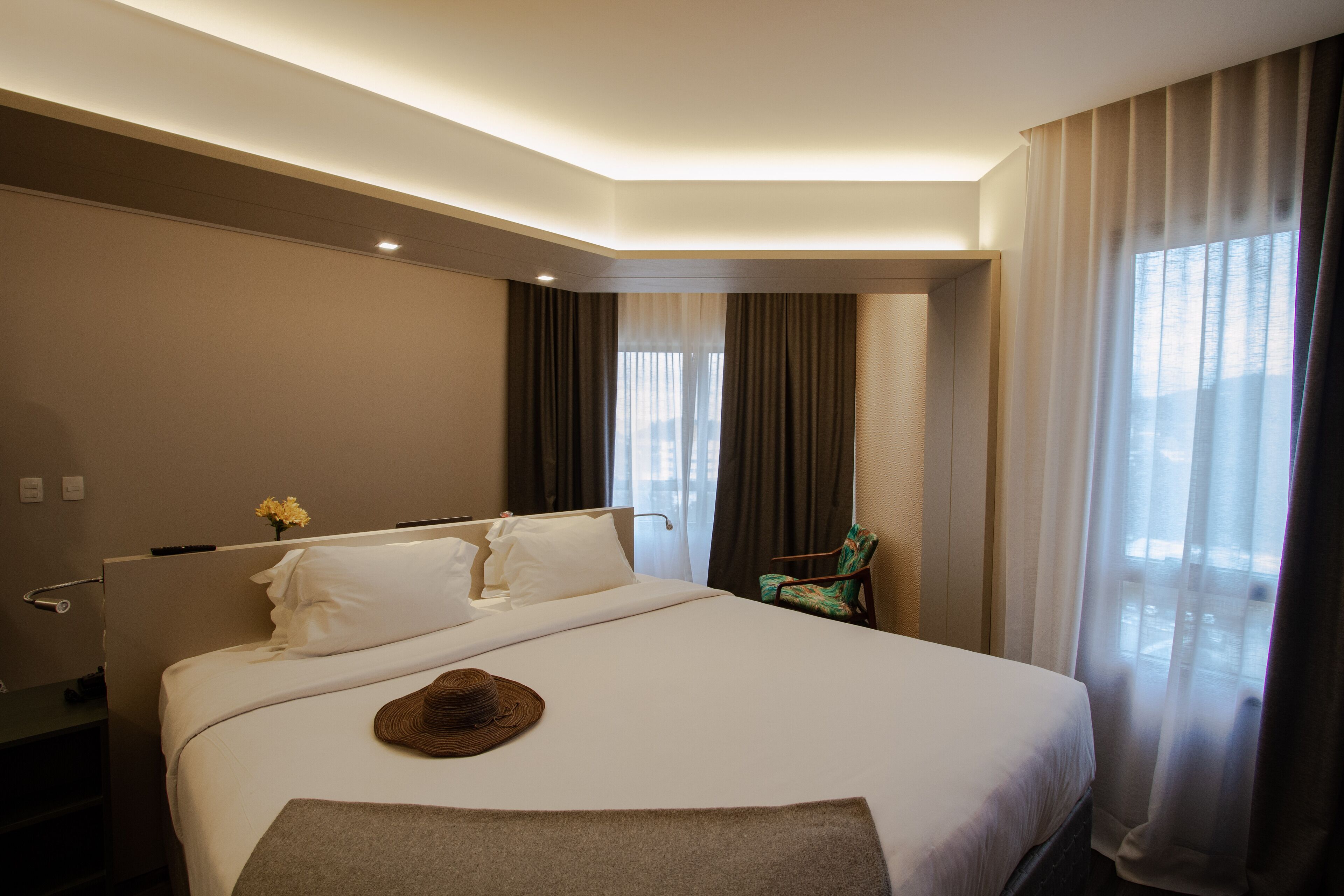 Ein Hotelzimmer mit einem großen Bett, einem Nachttisch, einem Sessel und einem Fenster mit Vorhängen.