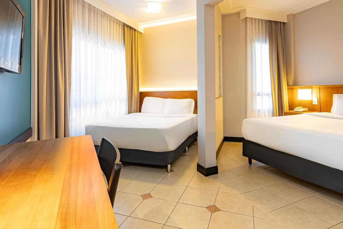 A hotel room with two beds, a desk, and a chair.
