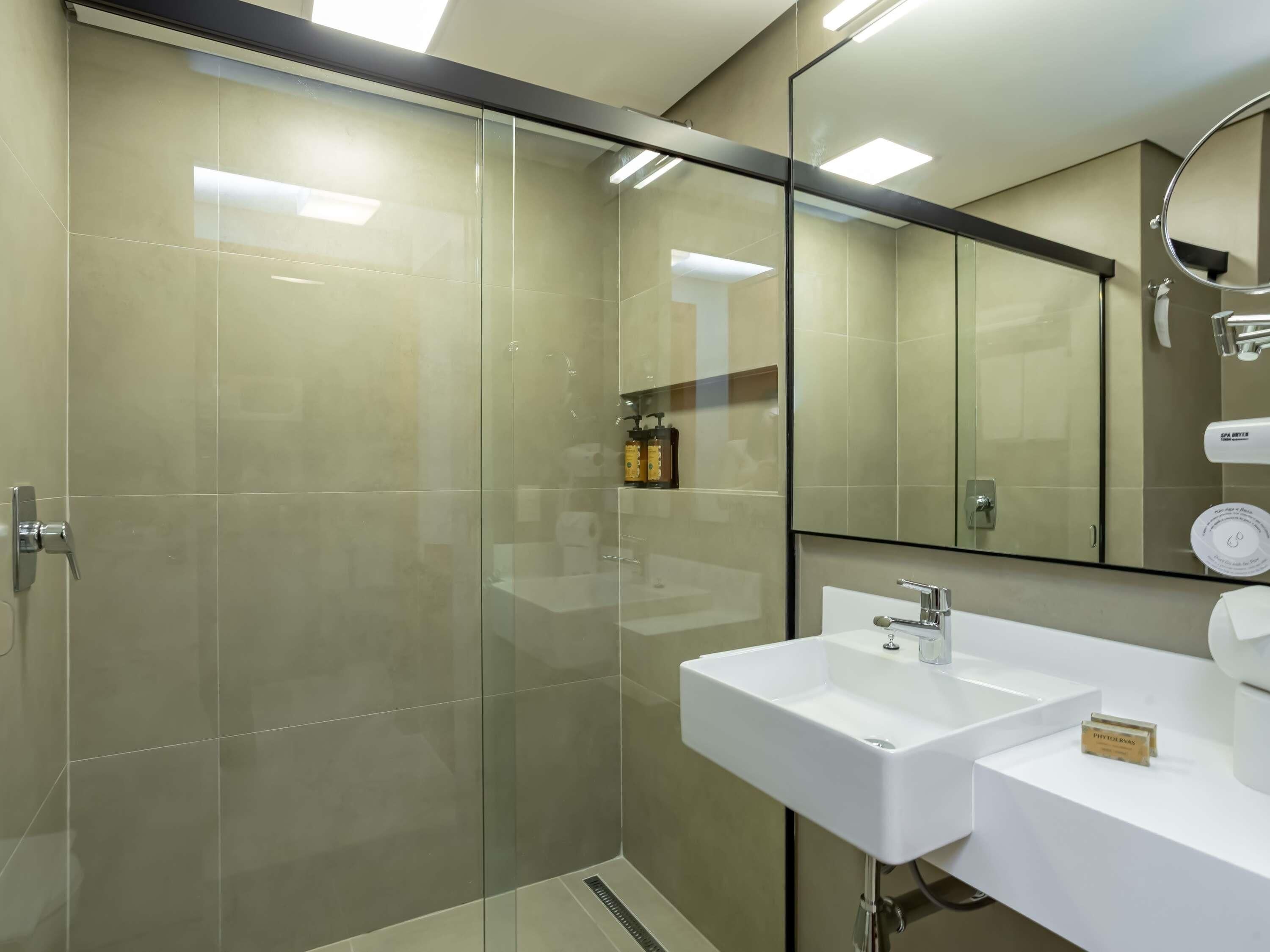 Un baño moderno con cabina de ducha de vidrio, un lavabo blanco y un espejo grande.