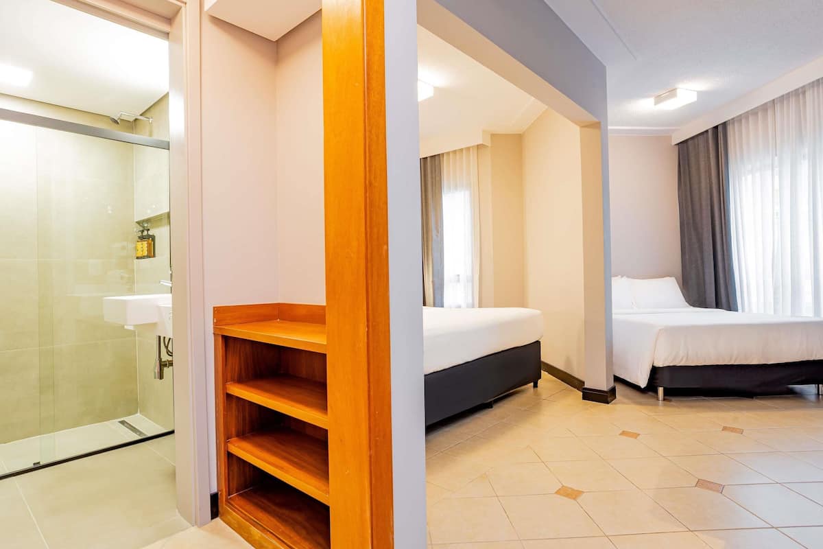 A hotel room with a shower, a bed, a bedside table, and a wooden shelf.