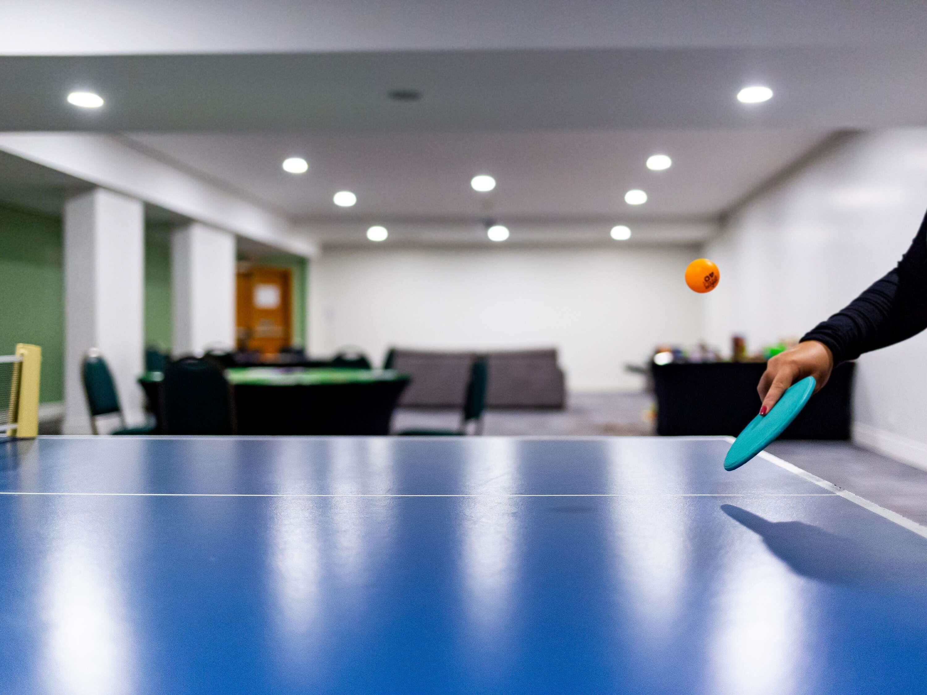A ping pong table in a room with a green wall, a desk, and chairs.