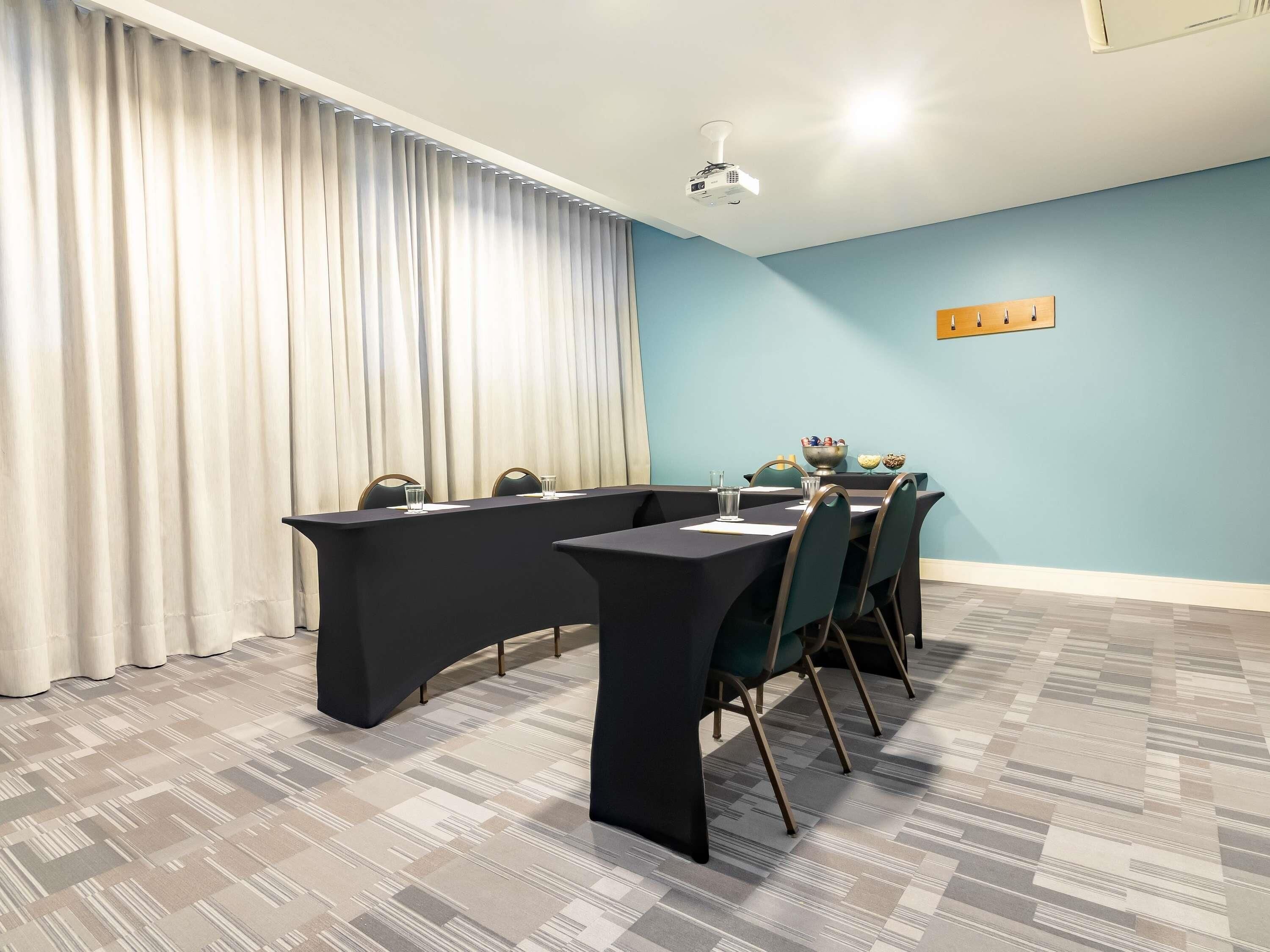 Un salón de conferencias con una larga mesa, sillas, un proyector y una pared azul claro.