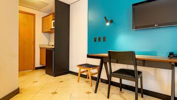 A modern room with a blue accent wall, a flat-screen TV mounted above a wooden desk, and a small stool.