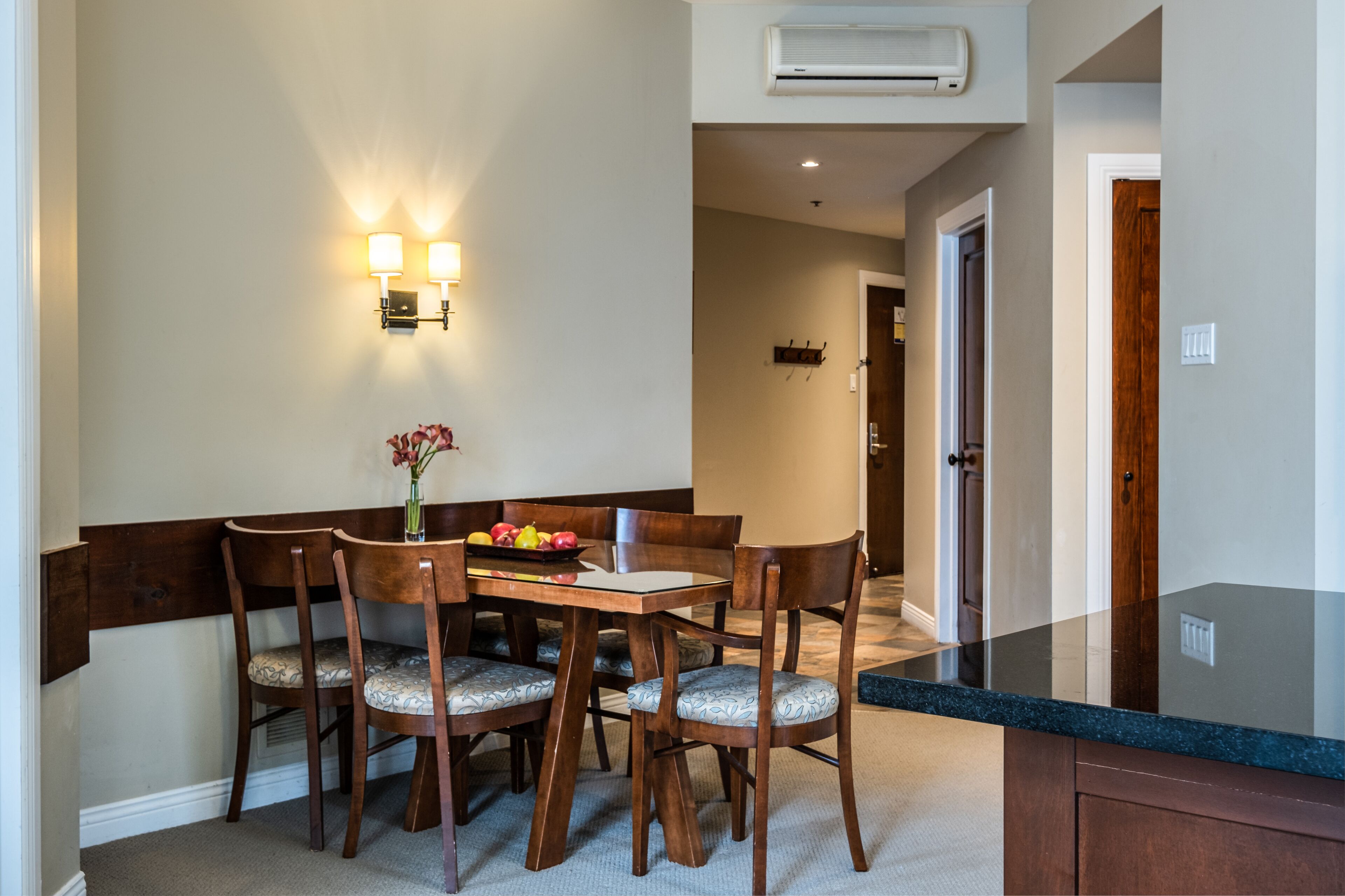 A dining area with a wooden table and chairs, a vase with flowers, and wall-mounted lighting.