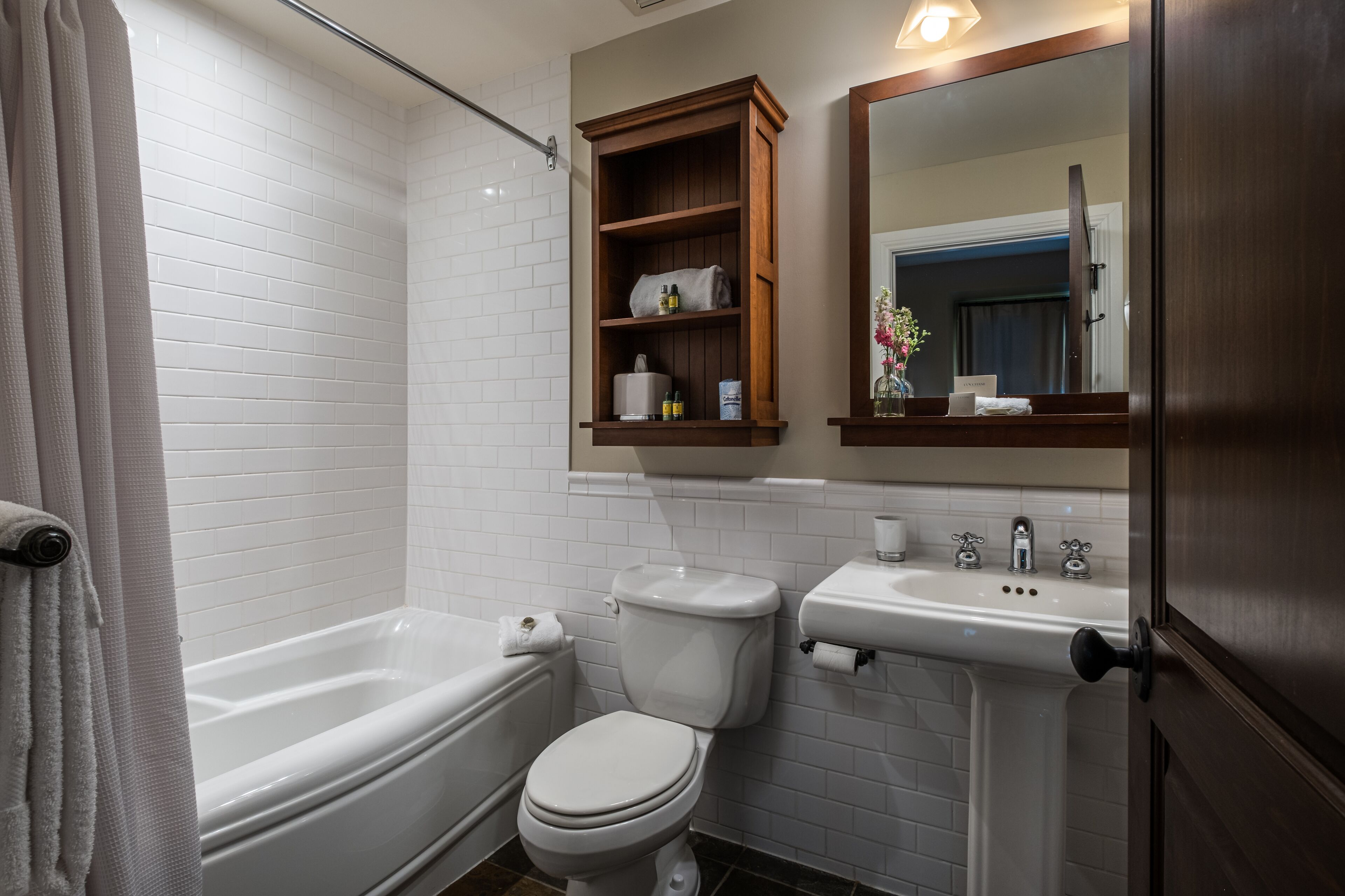 Ein Badezimmer mit Badewanne, Toilette, Waschbecken und einem hölzernen Medizinschränkchen über dem Waschbecken.