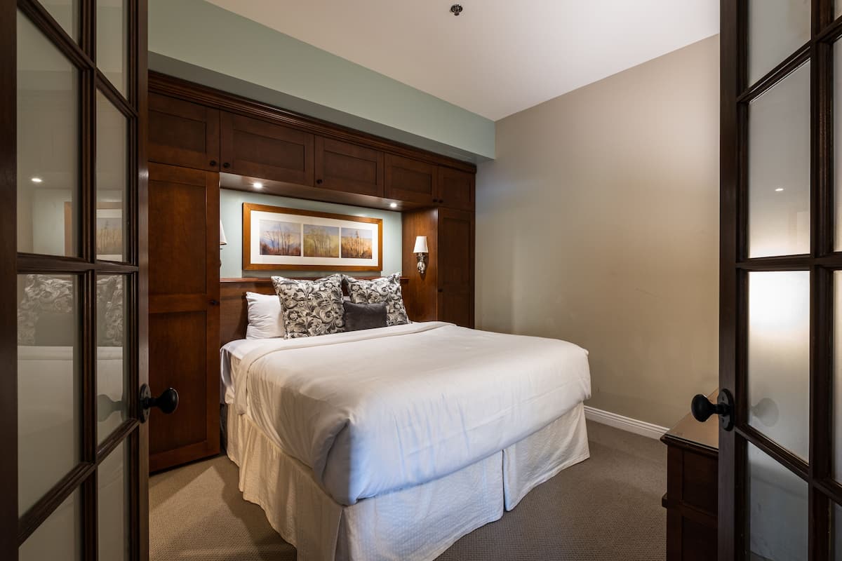 A bedroom with a large bed, wooden headboard, and a framed picture above the bed.