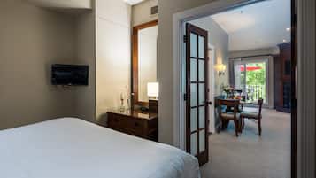 A hotel room with a bed, a TV, a desk with a chair, and a balcony with a table and chairs.