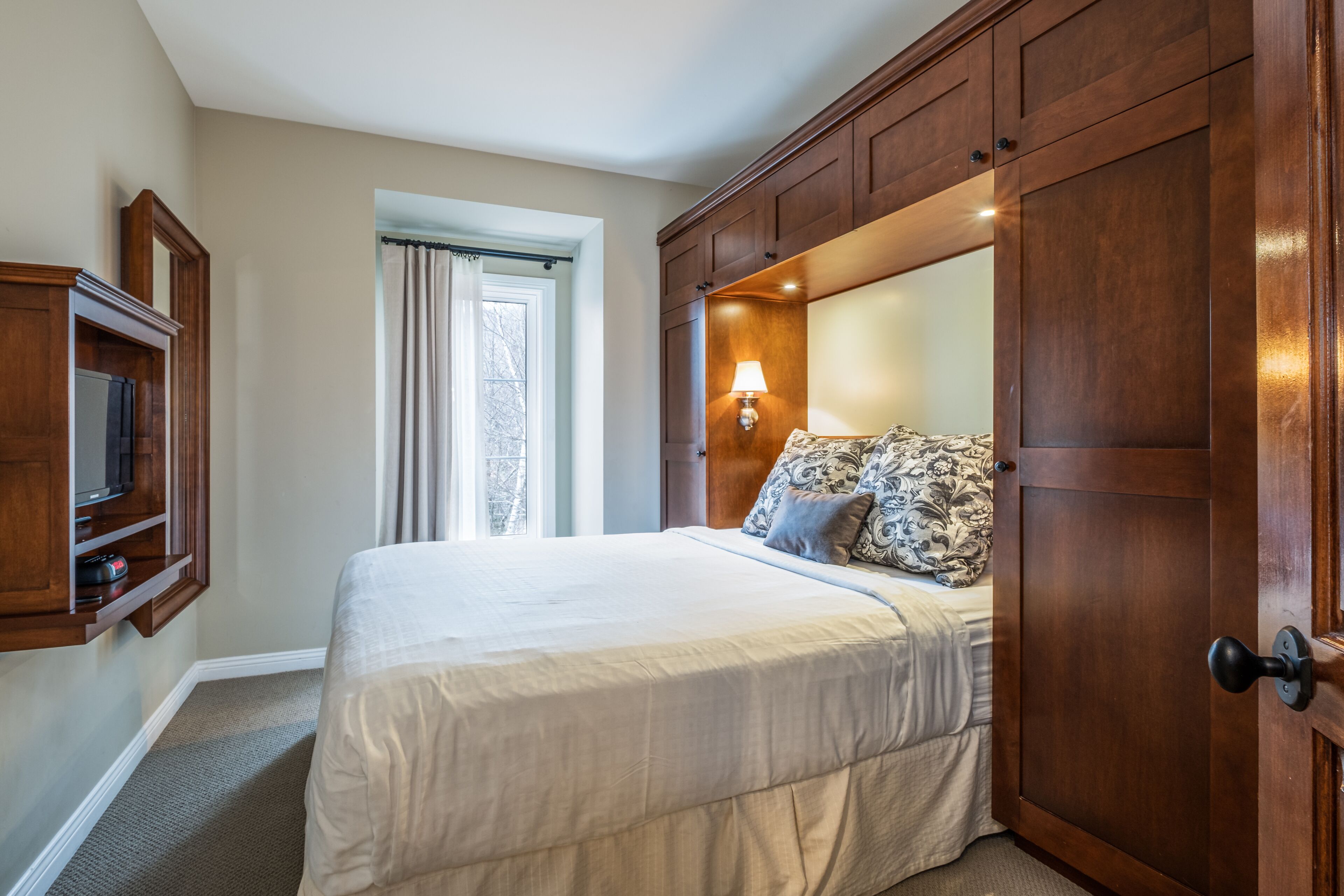 A hotel room with a large bed, a wooden wardrobe, a television, and a window with curtains.