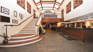 Un vestíbulo amplio con una imponente escalera, un mostrador de recepción y un techo alto con vigas de madera.