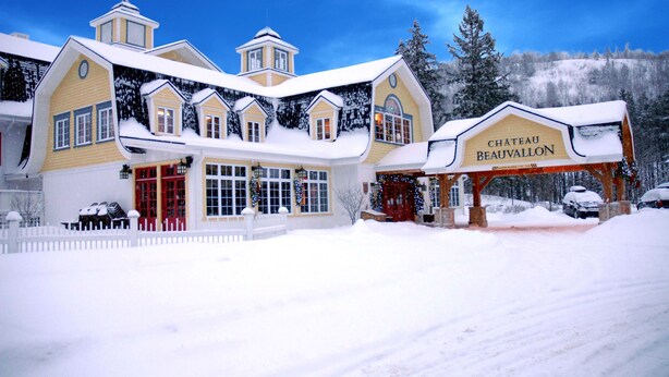 Un edificio grande de varios pisos con techo cubierto de nieve y un cartel que dice "CHATEAU BEAUVALON".