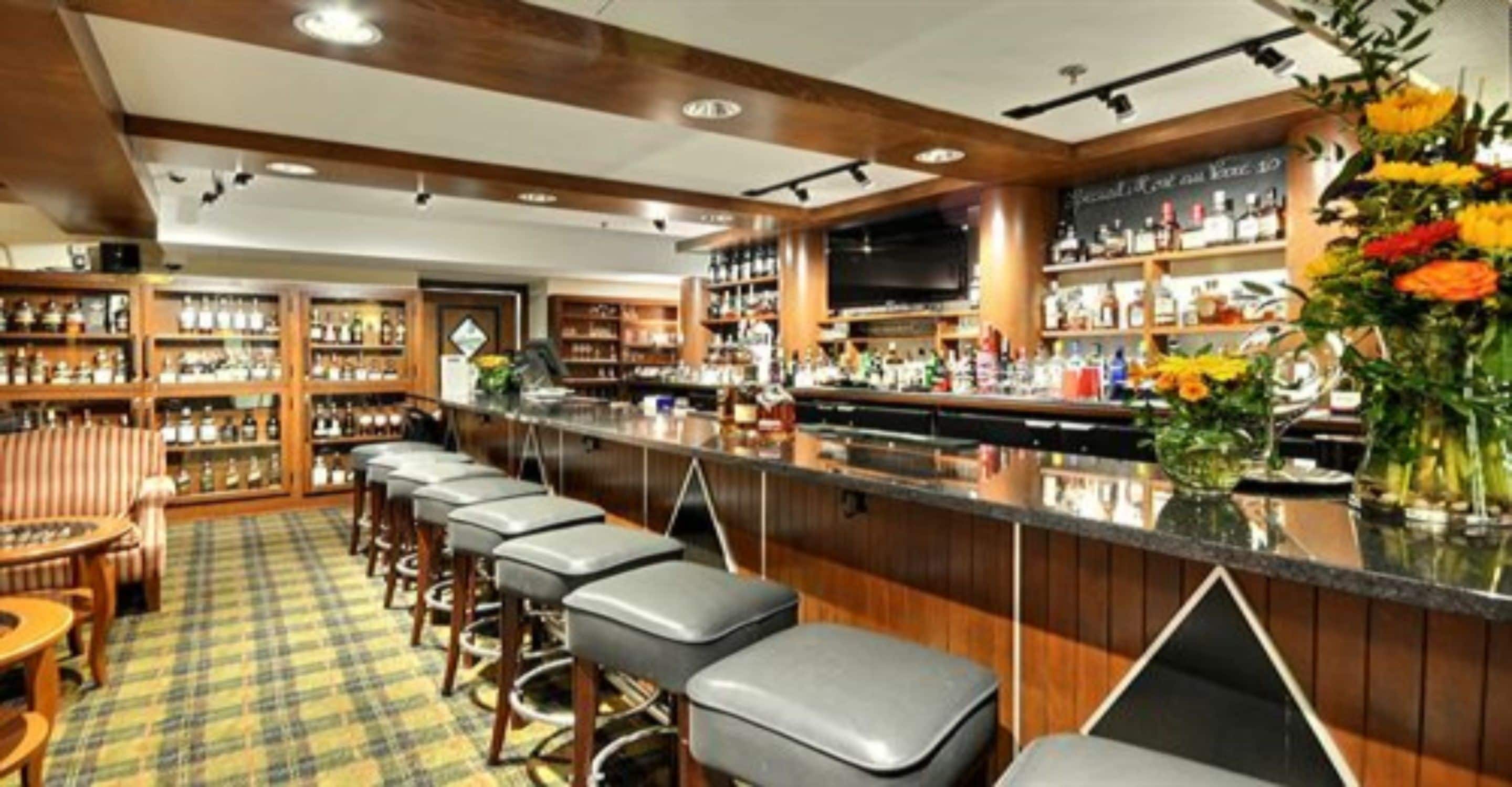 A bar area with wooden bar counters, stools, and shelves stocked with bottles.