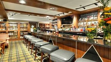 A bar area with wooden bar counters, stools, and shelves stocked with bottles.