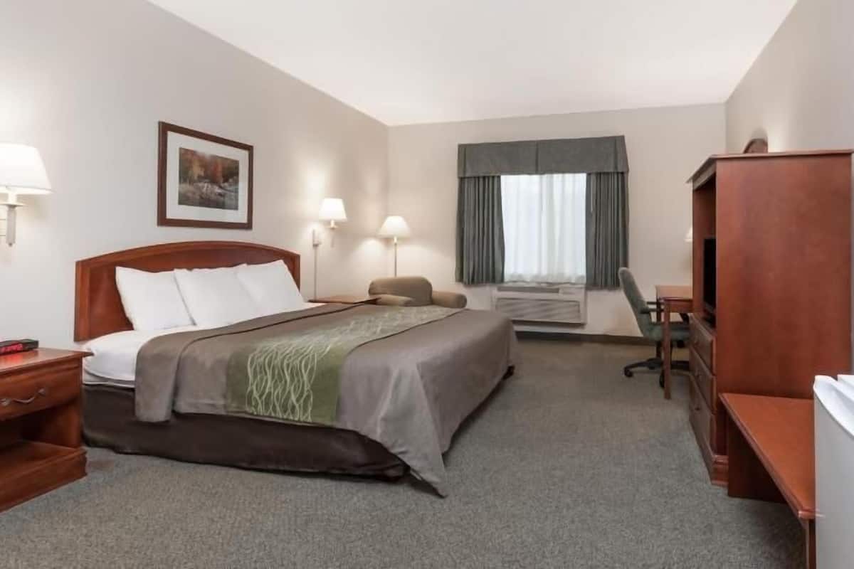 A hotel room with a bed, bedside tables, a desk, a chair, a television, and a window with curtains.