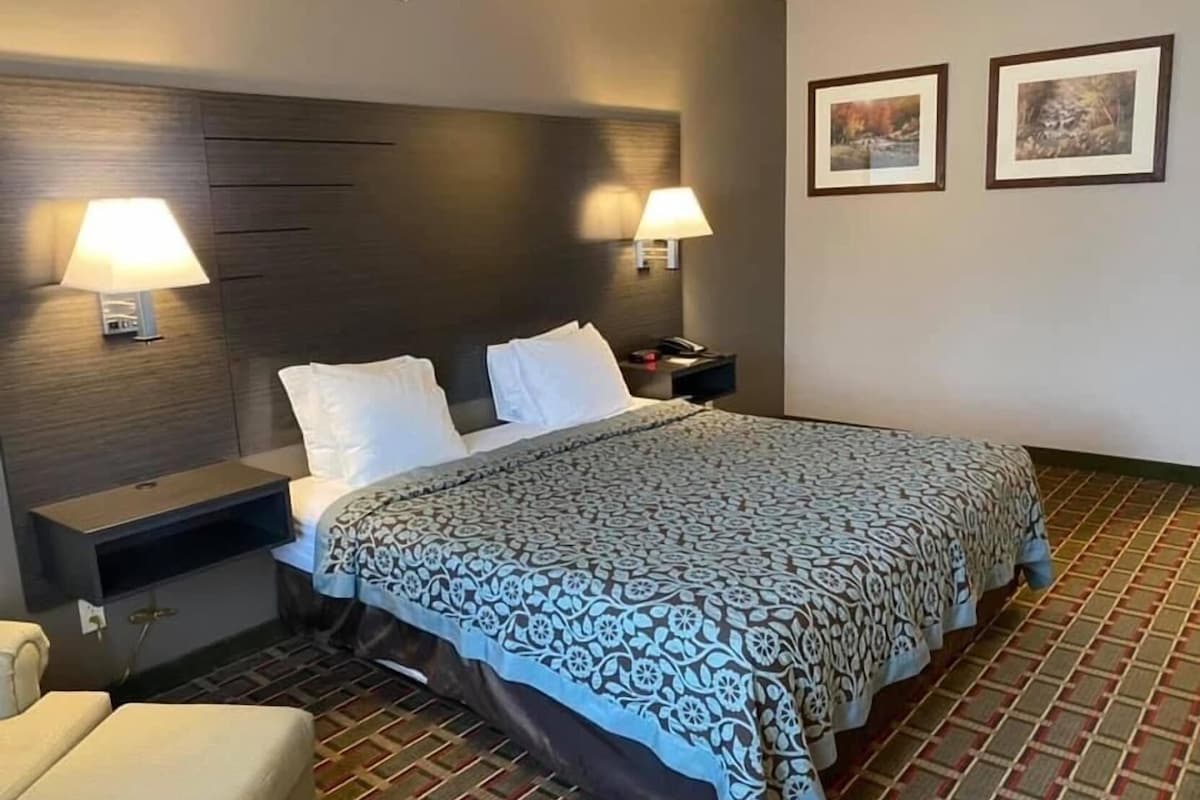 A hotel room with a bed, two bedside lamps, a nightstand, a chair, and two framed pictures on the wall.