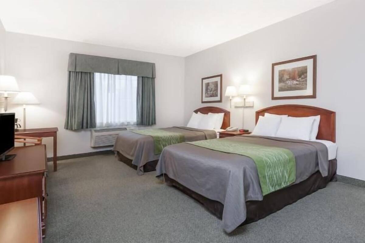 A hotel room with two beds, a desk, a TV, and a window with curtains.