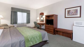Quarto de hotel com cama, escrivaninha, cadeira, televisão, frigorífico e um quadro na parede.