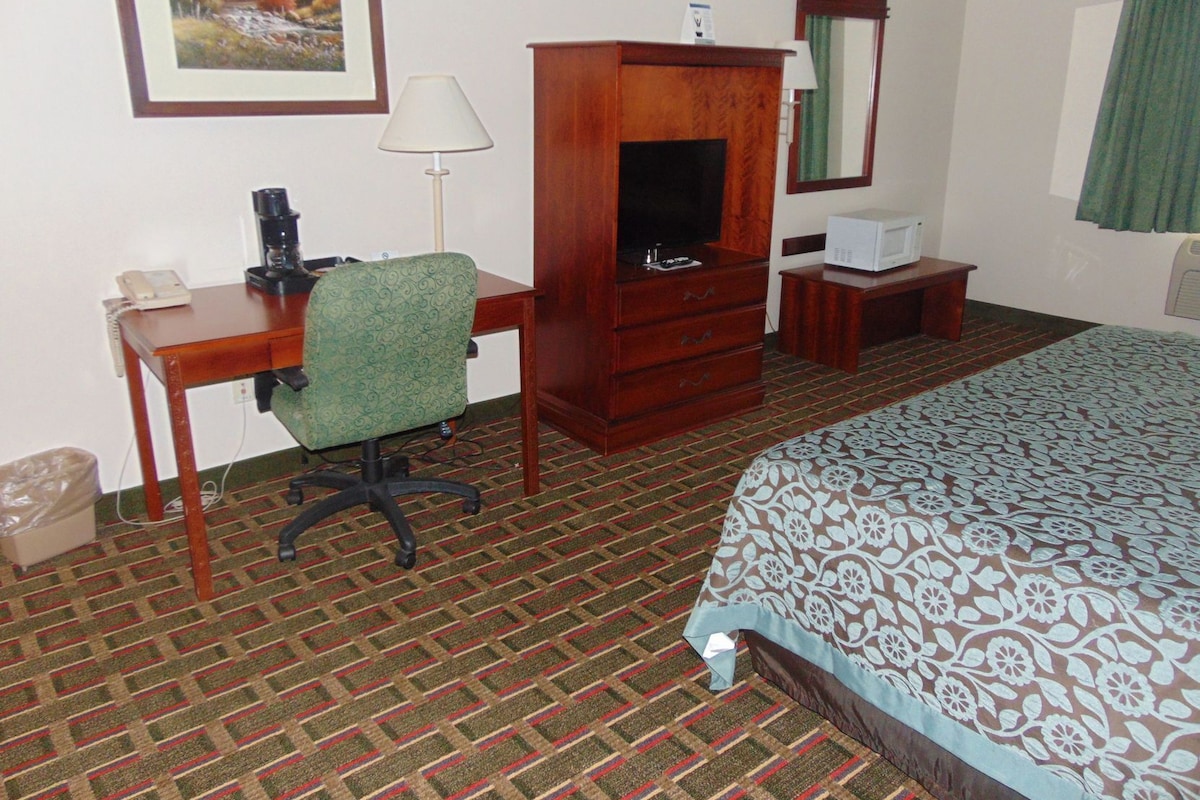 A hotel room with a bed, a desk with a telephone, a chair, a television, a dresser, a lamp, and a framed picture on the wall.