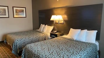 Habitación de hotel con dos camas, cada una con ropa de cama estampada, una mesita de noche con lámpara y cuadros en la pared.