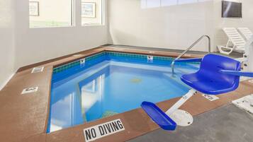 Una piscina interior con un cartel de 'NO DIVING', una silla azul y una escalera de piscina.