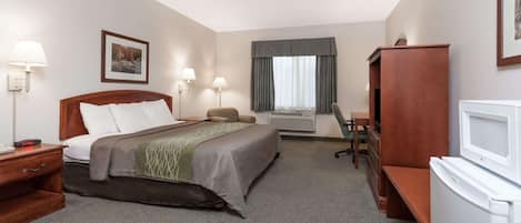 A hotel room with a bed, bedside table, lamp, desk, chair, and a television.