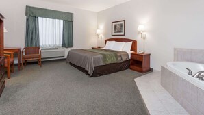 Una habitación de hotel con cama, escritorio, silla, ventana con cortinas, un cuadro en la pared, lámpara y bañera.