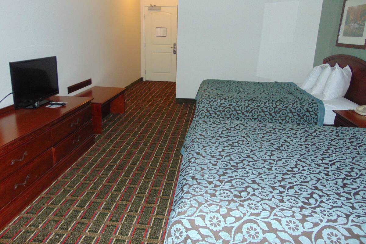 A hotel room with a bed, a television on a dresser, and a door in the background.