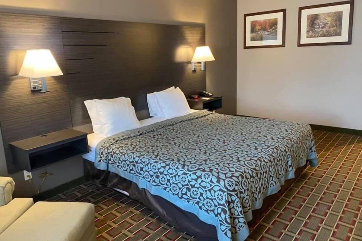 A hotel room with a large bed, two bedside lamps, a nightstand, a chair, and two framed pictures on the wall.