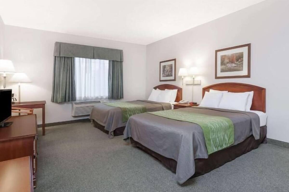 A hotel room with two beds, a desk, a television, and a window with curtains.