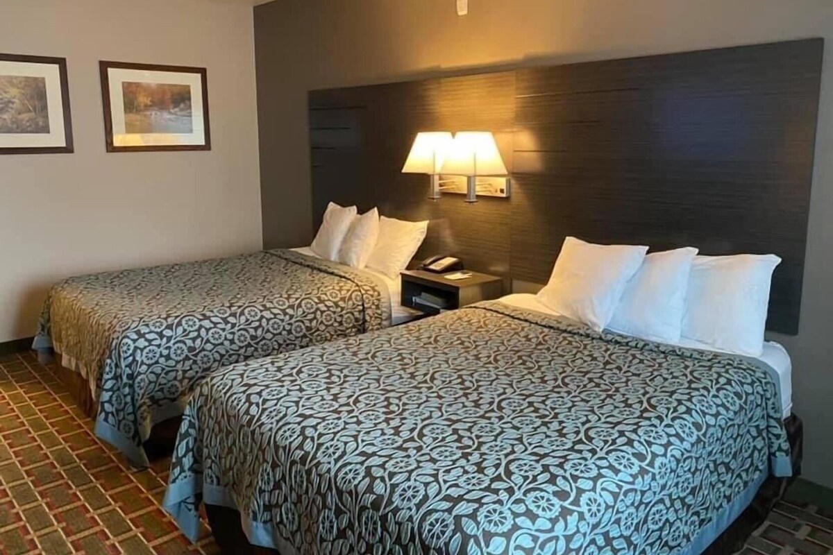 A hotel room with two beds, a nightstand with a lamp, and framed pictures on the wall.