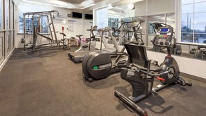 Un gimnasio con diferentes equipos de ejercicio, ventanas amplias y un muro de espejos.