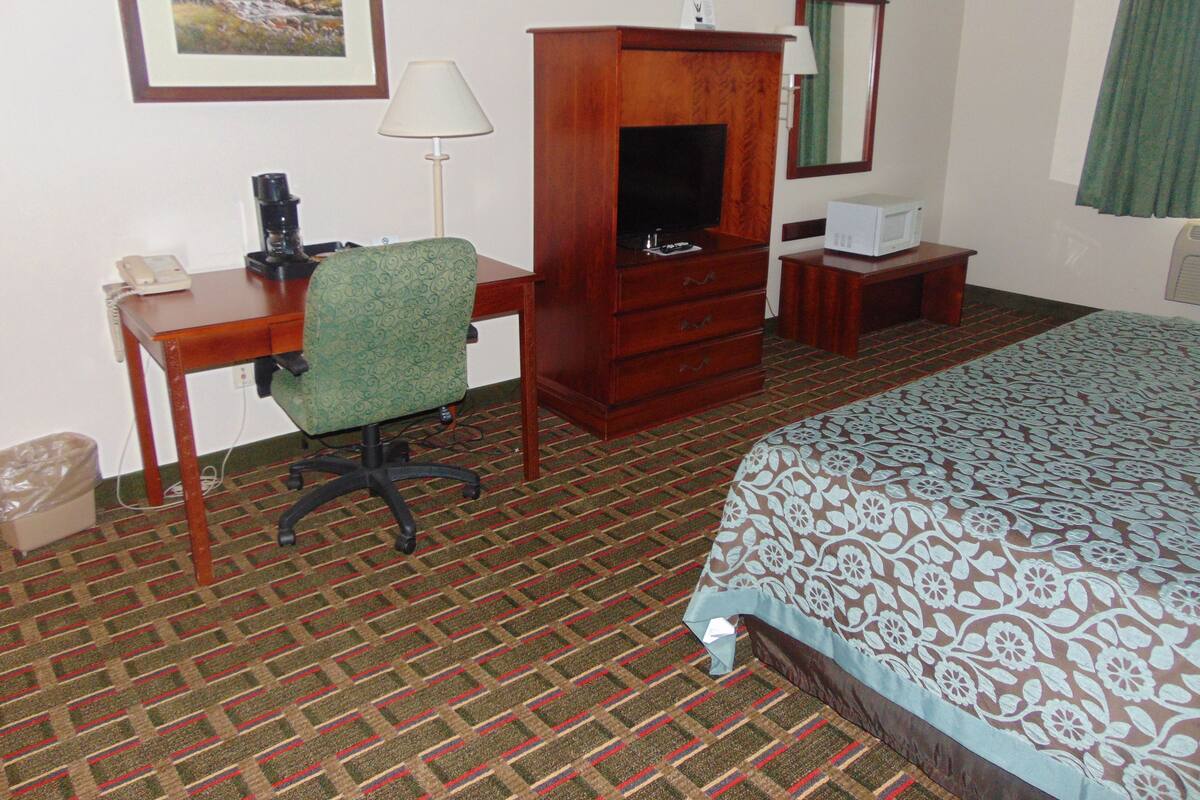 A hotel room with a bed, a desk with a chair, a television, a small table, a mirror, and a picture on the wall.