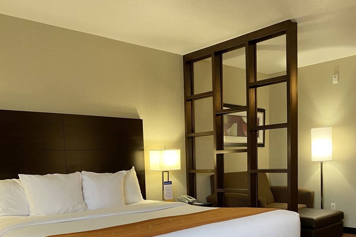 A hotel room with a large bed, a wooden headboard, two bedside lamps, a nightstand, and a carpeted floor.
