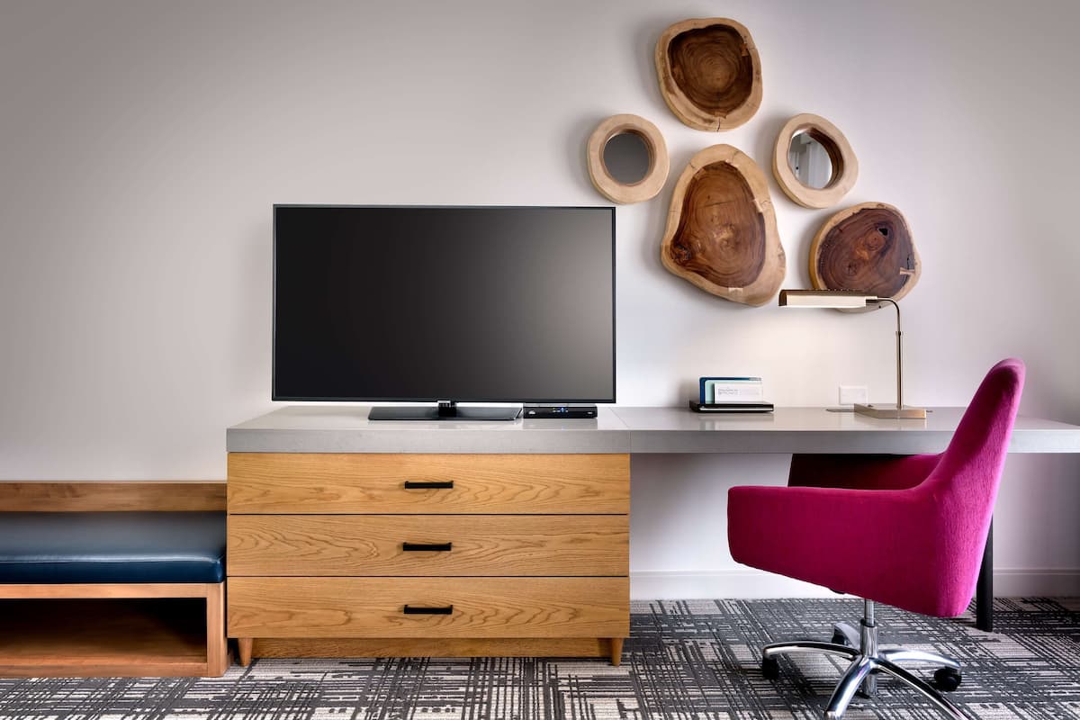 A modern office space with a flat-screen TV, wooden drawers, a desk, a pink chair, and wooden wall art.