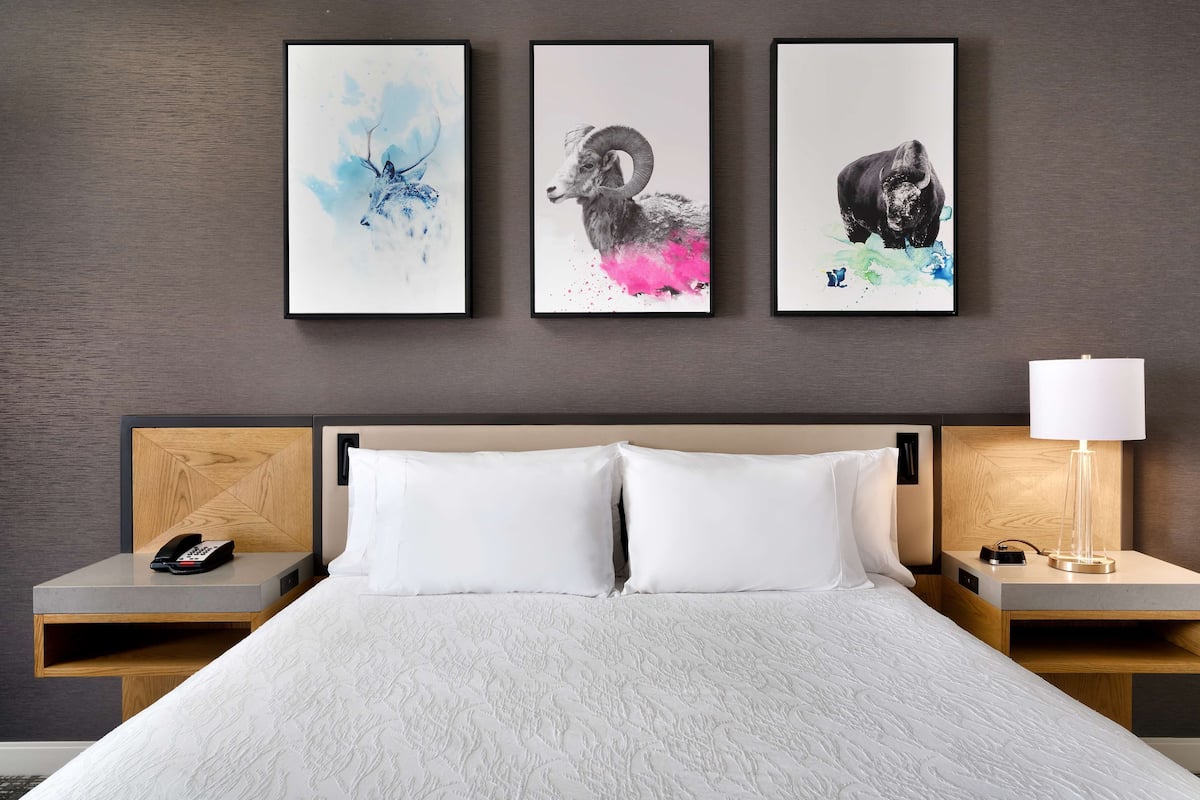 A hotel room with a bed, two nightstands, a lamp, and three artworks on the wall.
