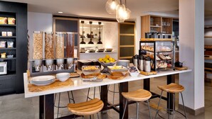 A modern kitchen with a central island, bar stools, and various food items. - Hilton Garden Inn Bozeman (Bozeman)