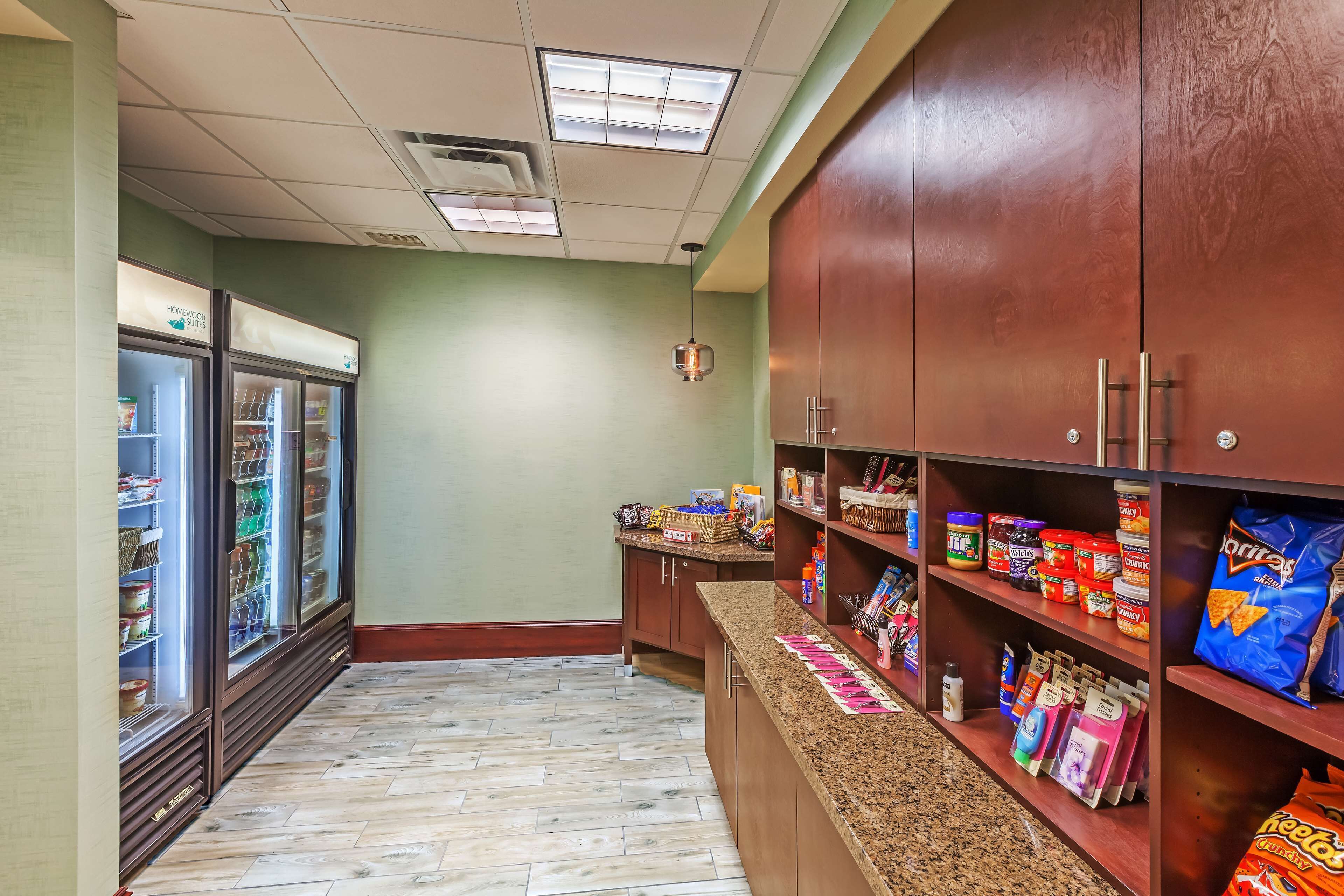 A kitchenette with a refrigerator, pantry, and shelves stocked with snacks and condiments.