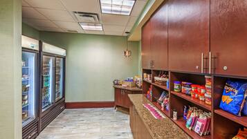 A kitchenette with a refrigerator, pantry, and shelves stocked with snacks and condiments.