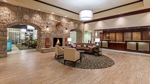 A spacious lobby with a stone archway, a fireplace, a reception desk, and a seating area with a patterned rug. - Homewood Suites by Hilton Wichita Falls (Wichita Falls)