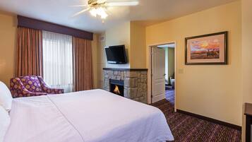 A hotel room with a bed, a fireplace, a television, a door leading to another room, and a framed picture on the wall.
