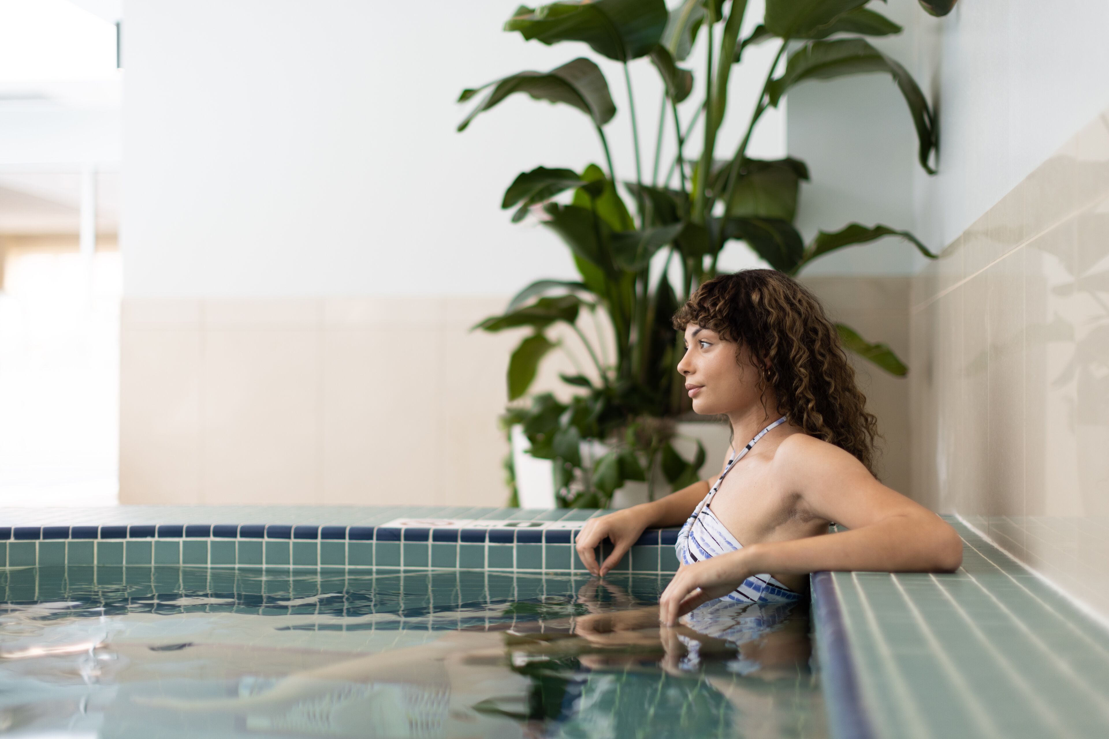 Una persona relajándose en un jacuzzi pequeño y con azulejos, con una planta de fondo.