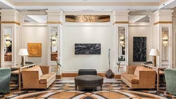 A spacious lobby with a large chandelier, two sofas, a round ottoman, and a marble floor.