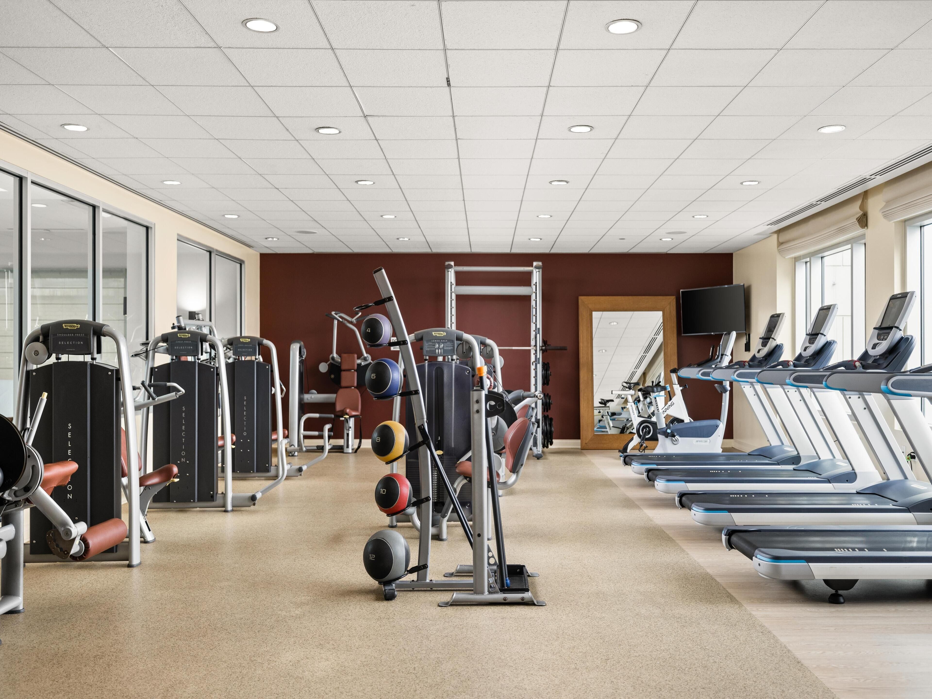 Un gimnasio con cintas de correr, máquinas de pesas y un espejo.