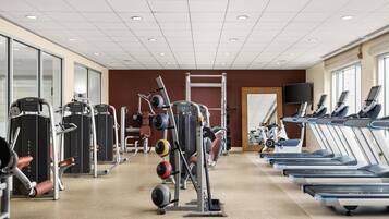 Un gimnasio con cintas de correr, máquinas de pesas y un espejo.