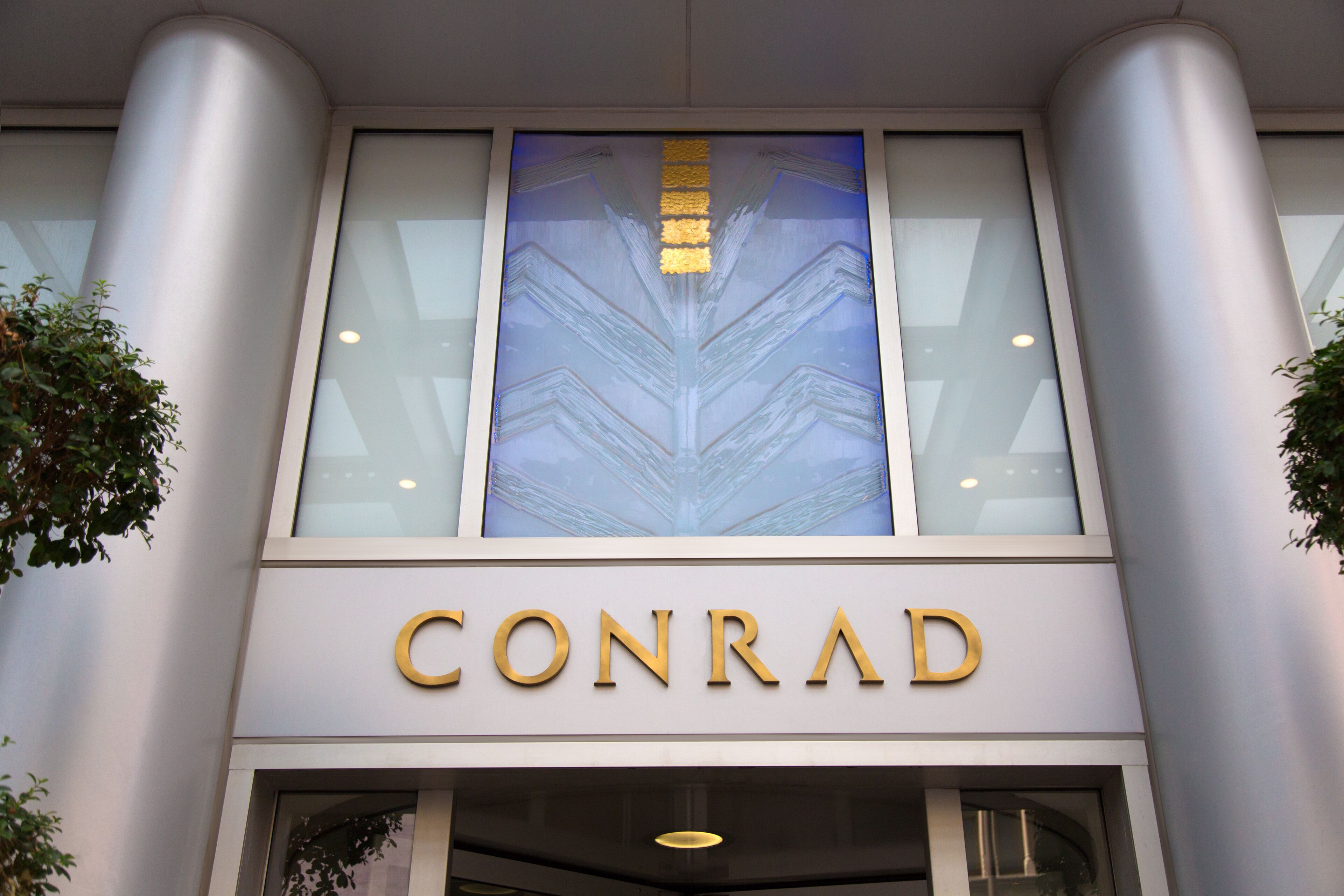 Exterior de um edifício com o nome 'CONRAD' em destaque em letras douradas.